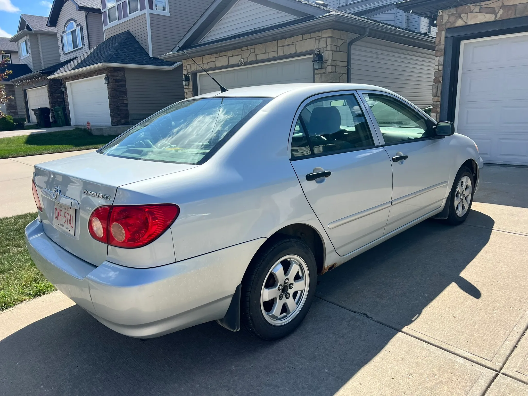 Silver Toyota Corolla in Alberta driveway under clear blue sky; suburban homes, garages, and lawns in background.