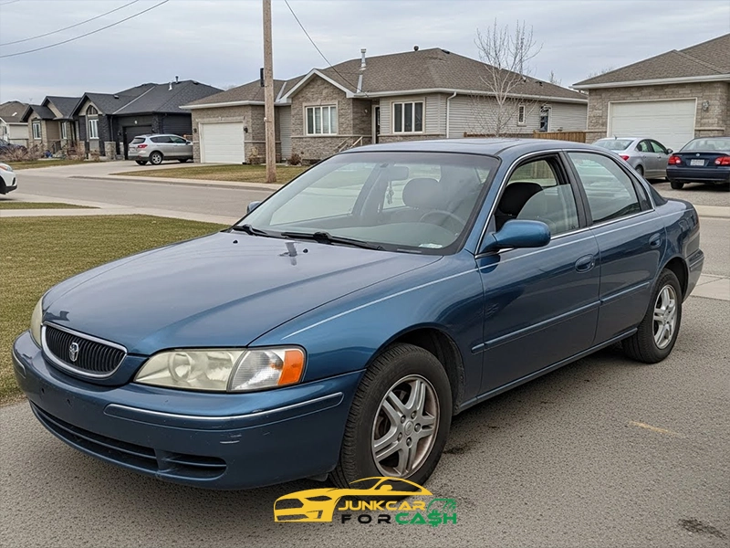 Blue four-door sedan parked on a residential street in a suburban neighborhood, shown from a front-side angle with houses and driveways in the background.