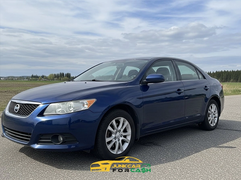 Blue four-door sedan parked on a paved road with open fields and a cloudy sky in the background.