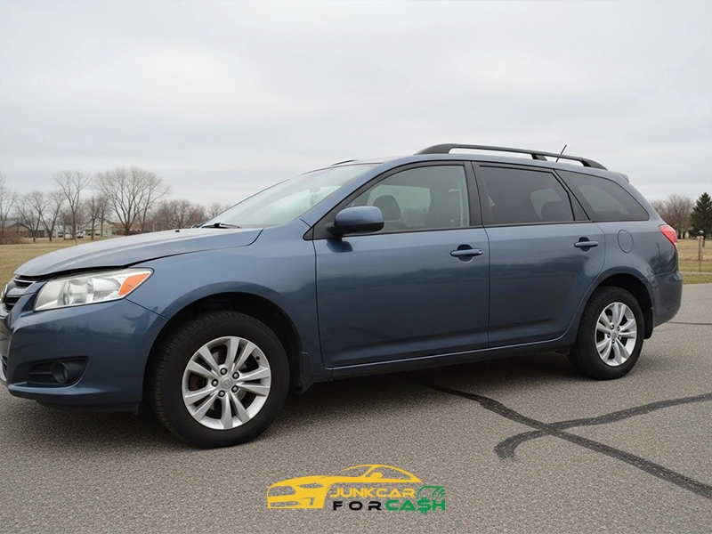 Blue station wagon parked on an empty paved lot with bare trees and an overcast sky in the background.